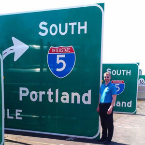 Navjoy employee stands next to large highway traffic signs