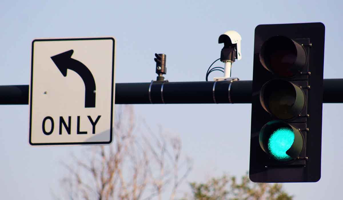 Camera mounted on a traffic signal pole next to a traffic signal showing a red light.